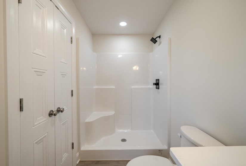 White shower stall with an integrated bench seat, black fixtures, and recessed lighting
