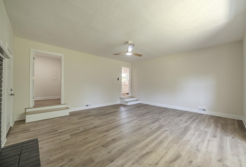 Spacious living area featuring wood-finish flooring, a ceiling fan with integrated lighting, and neutral wall tones