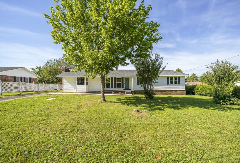 White siding exterior with dark shutters, a covered porch entry, and a prominent mature tree