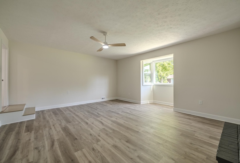 Spacious room featuring wood-finish flooring, a contemporary ceiling fan, and a large window with white trim