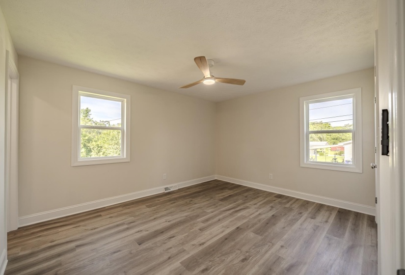 Spacious room featuring wood-finish flooring, neutral wall tones, two windows with white trim, and a contemporary ceiling fan with integrated lighting