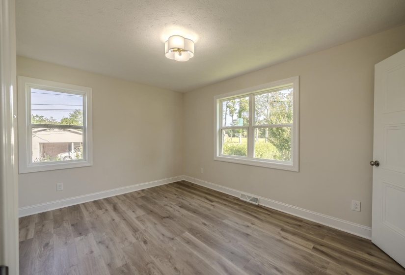 Neutral-toned interior room featuring wood-finish flooring, two windows with white trim, and a contemporary ceiling light fixture