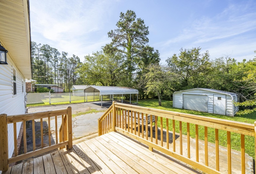 Spacious wood-finish deck overlooking a large lot with a metal carport, detached garage, and mature trees