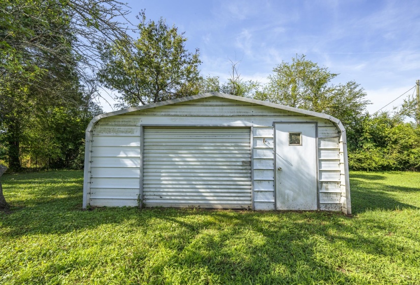 Detached metal outbuilding featuring a roll-up garage door, an entry door with a small window, and a surrounding grass lawn