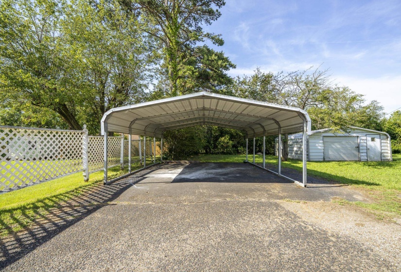 Metal carport structure with an asphalt driveway and a lattice fence