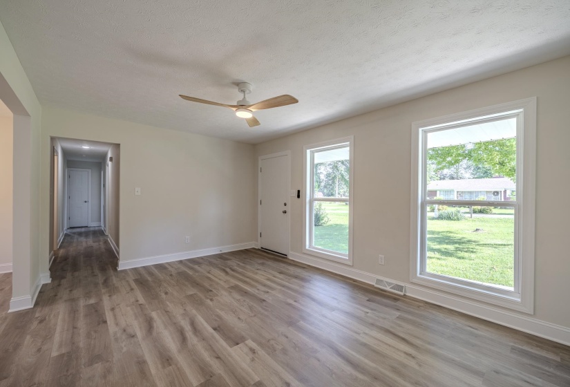 Spacious room featuring wood-finish flooring, two large windows, a ceiling fan with light, white trim, and a white entry door