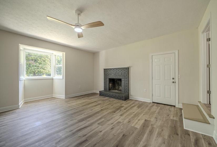 Spacious room featuring wood-finish flooring, a contemporary ceiling fan with integrated lighting, and a brick fireplace