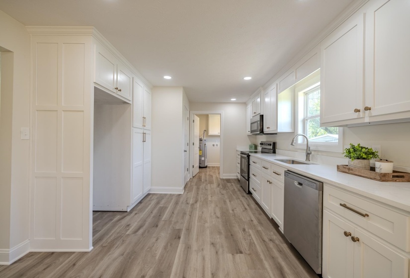 Modern kitchen featuring white shaker cabinetry, stainless steel appliances, light-toned countertops, wood-finish flooring, and recessed lighting