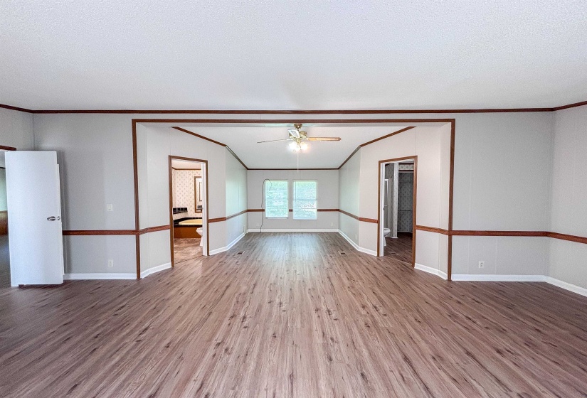 Spacious interior featuring wood-finish flooring, light grey walls with wood trim, and a ceiling fan