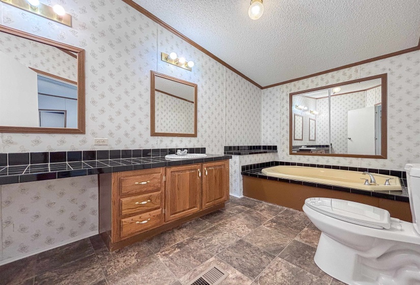 Bathroom featuring a built-in tub with tile surround, wood-finish vanity with dual sinks, and tile flooring