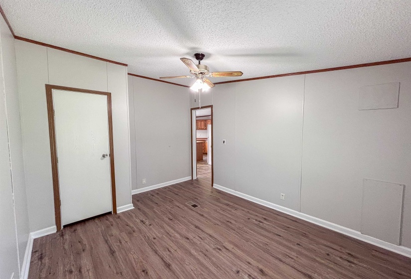 Spacious room featuring wood-finish flooring, light gray wall panels, white baseboards, and a ceiling fan with light fixture