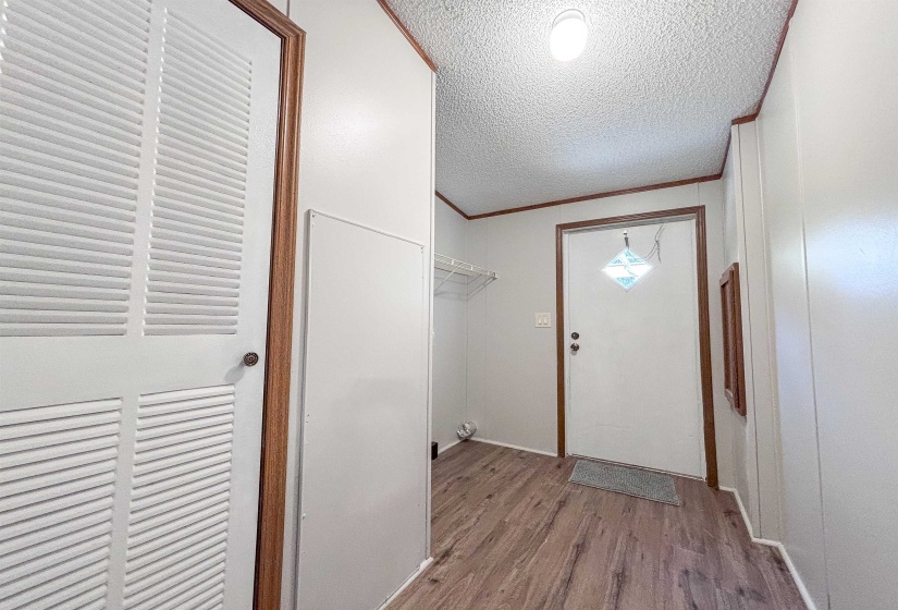 Entryway featuring wood-finish flooring, white paneled walls, and a white front door with decorative glass inlay