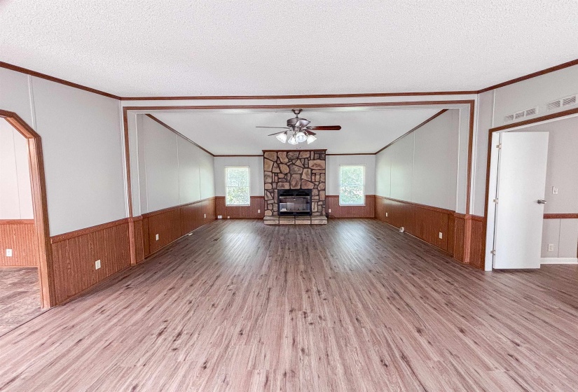 Spacious living area featuring wood-finish flooring, a stone fireplace, and wainscoting