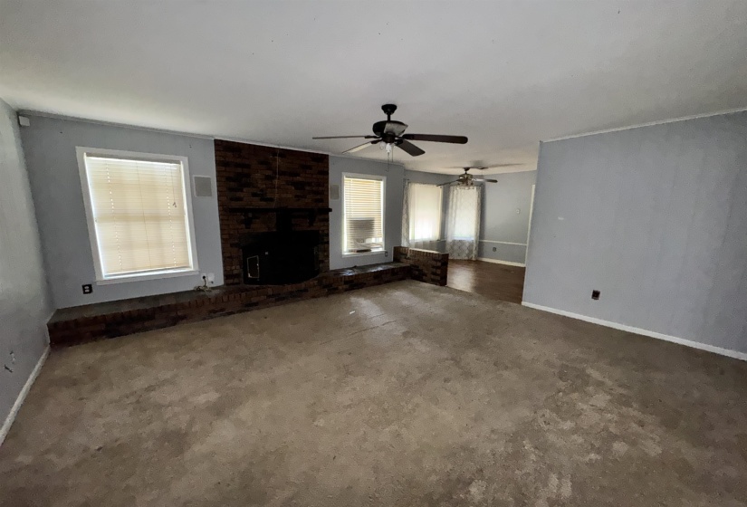 Living area featuring a brick fireplace with a raised hearth, multiple windows, and two ceiling fans