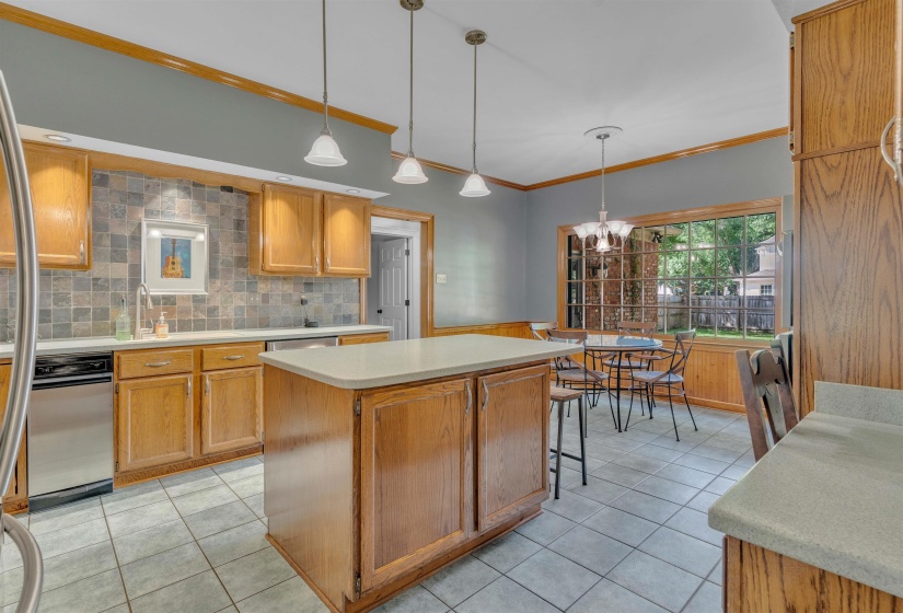 Kitchen featuring wood cabinetry, a center island with a light-toned countertop, a tile backsplash, stainless steel appliances, and tile flooring