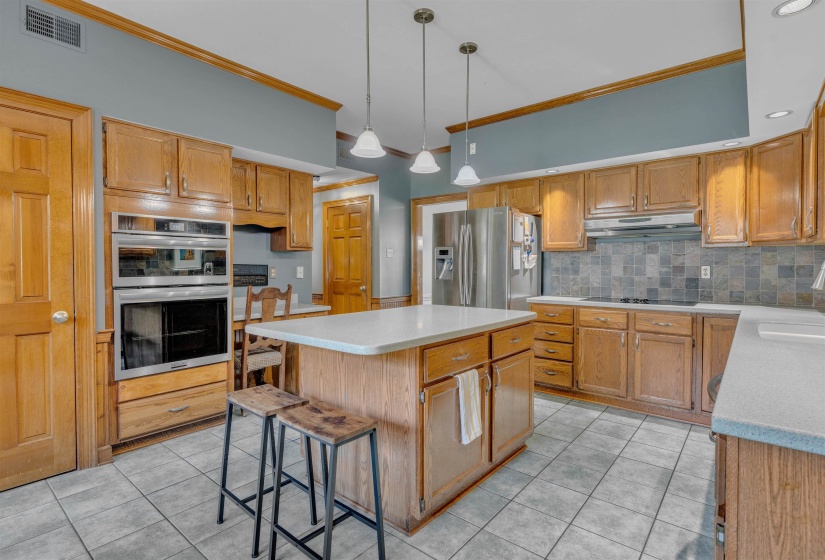 Kitchen featuring a central island with a light-toned countertop, tile flooring, wood-finish cabinetry, stainless steel appliances, and pendant lighting