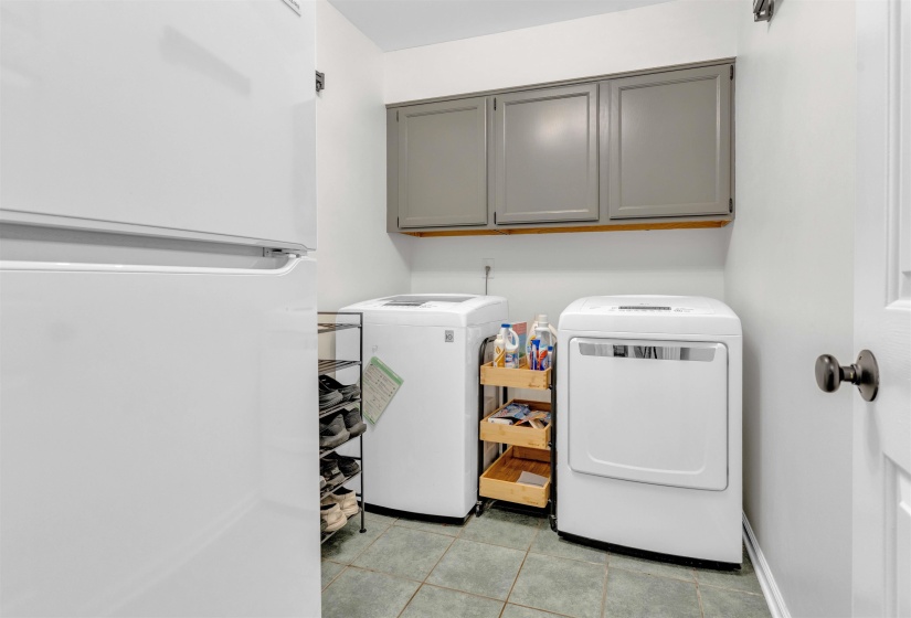 Dedicated laundry space featuring gray shaker-style cabinetry, tile flooring, and a white paneled door with dark hardware