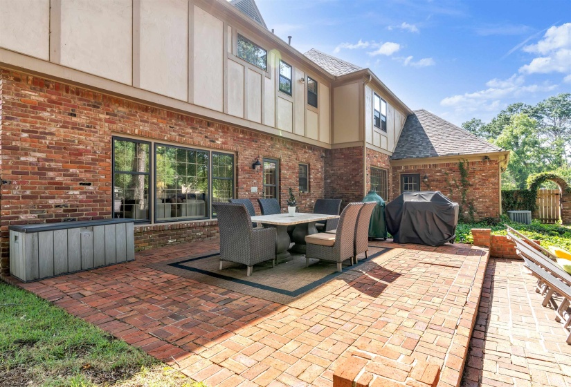 Expansive brick paver patio featuring a dining area, a brick and stucco exterior, and multi-pane windows