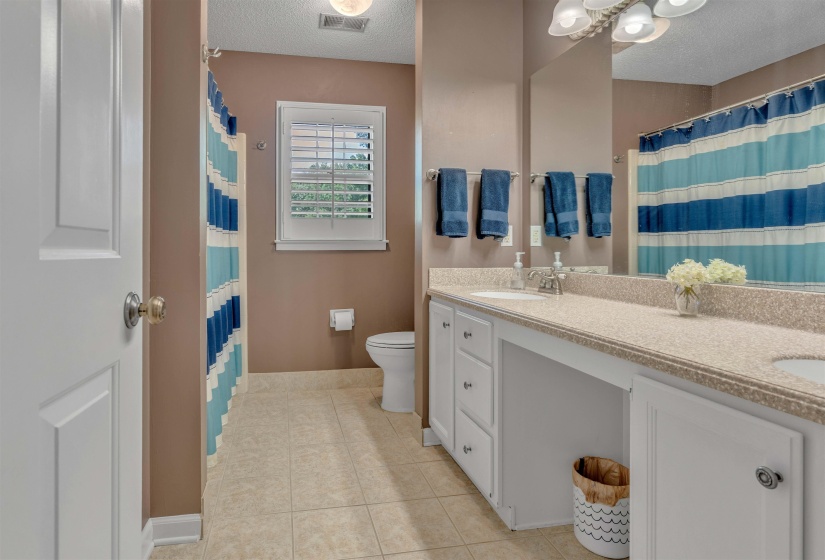 Bathroom featuring a dual-sink vanity with light-toned countertop, white cabinetry, and tile flooring