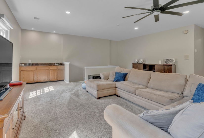 Carpeted room featuring a built-in wood-finish cabinet with a stone-finish countertop, recessed lighting, and a contemporary ceiling fan