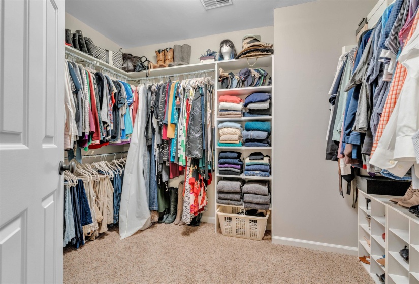 Spacious walk-in closet featuring built-in shelving, multiple hanging rods, durable carpet flooring, and a crisp white paneled door