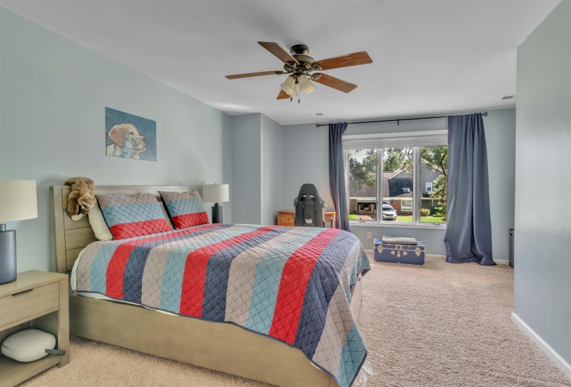 Spacious room featuring light blue walls, a large window with blue drapery, a ceiling fan with light fixture, and plush carpet flooring
