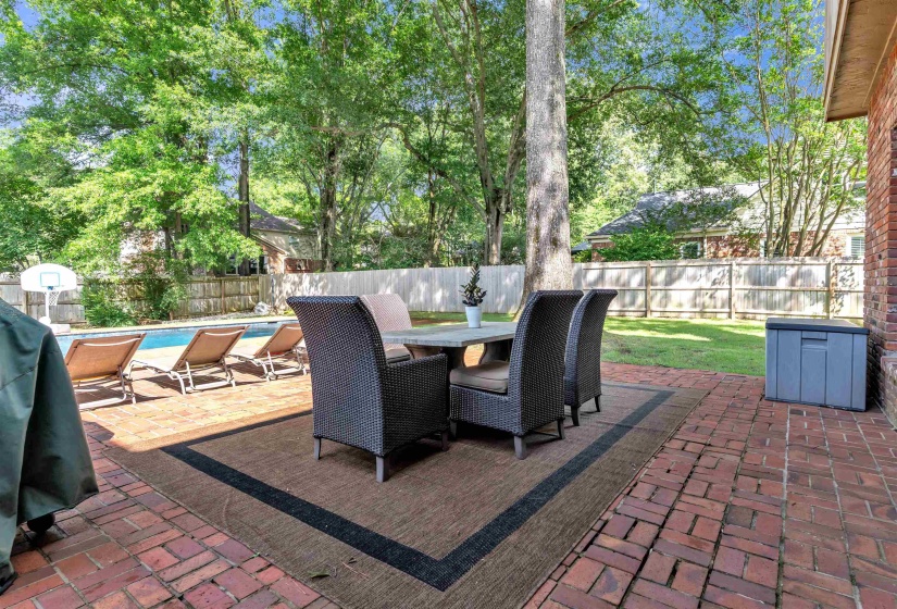 Brick patio with a dining area, a swimming pool, and a fenced backyard