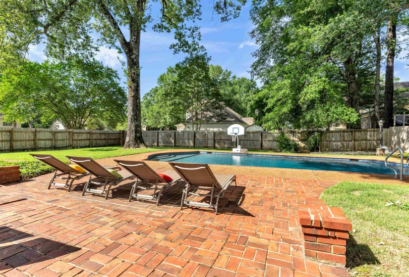 Curved swimming pool featuring a brick paver surround, a basketball hoop, and established perimeter fencing
