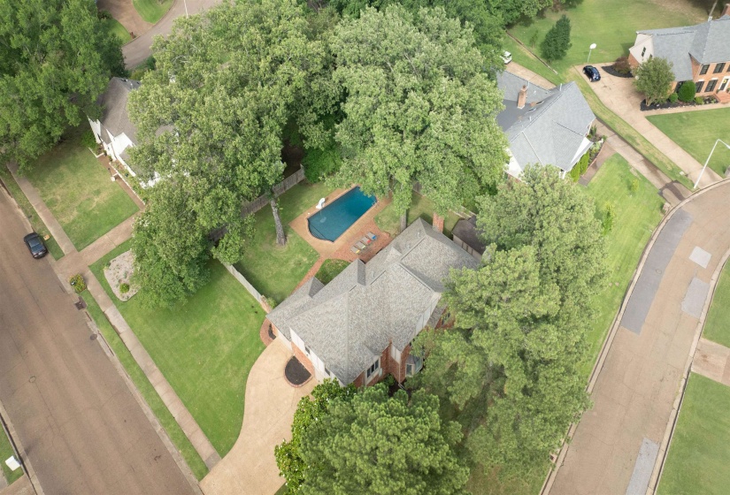 Aerial perspective showcasing a property with a private swimming pool, surrounded by mature trees, a manicured lawn, and paved roadways