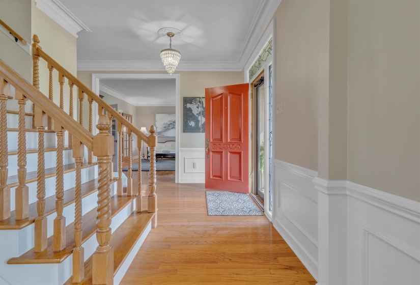 Entryway featuring wood-finish flooring, a red paneled front door, white wainscoting, and a crystal chandelier