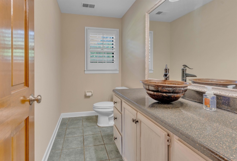 Powder room featuring a vessel sink with a dark bronze faucet, a vanity with a dark speckled countertop, and a window with white louvered shutters