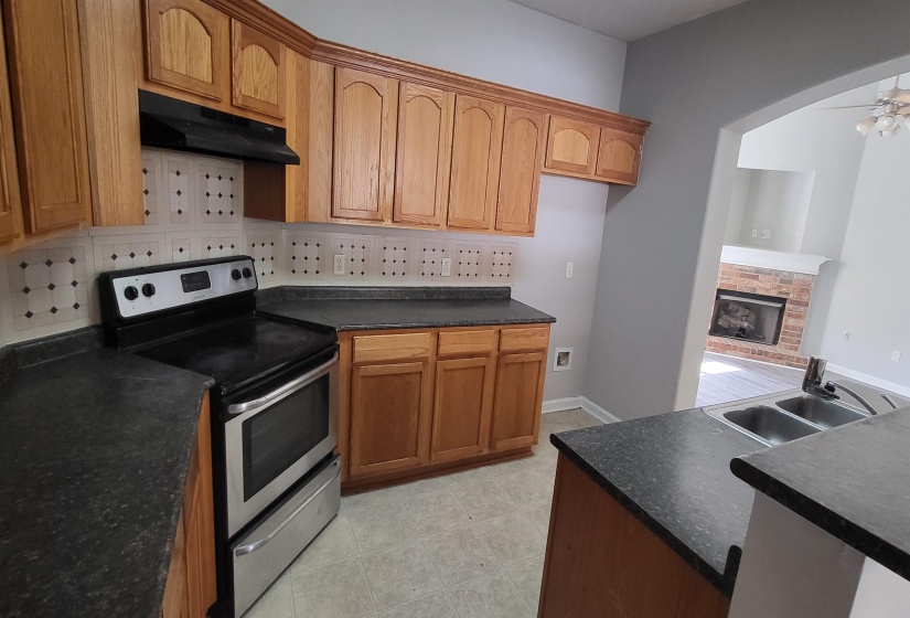 Kitchen featuring backsplash, electric stove, sink, a brick fireplace, and ceiling fan
