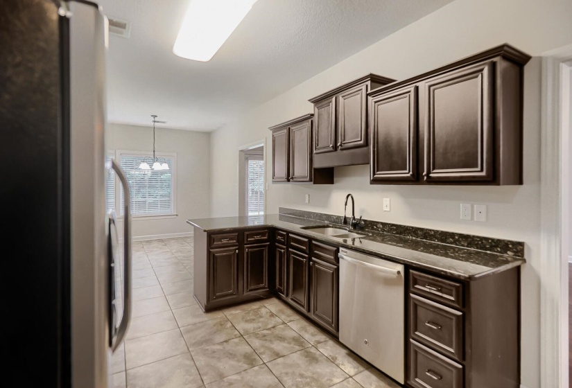 Kitchen featuring dark wood cabinetry, granite countertops, tile flooring, and stainless steel appliances