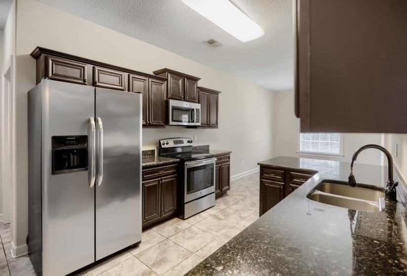 Kitchen featuring dark wood cabinetry, stainless steel appliances, speckled stone countertops, and tile flooring