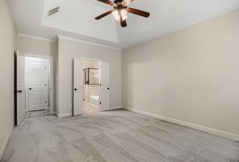 Spacious room featuring vaulted ceiling, crown molding, light-toned carpeting, and a ceiling fan