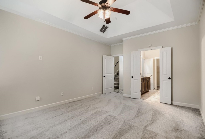 Spacious room featuring a tray ceiling, ceiling fan with light fixture, light gray carpeting, and white trim