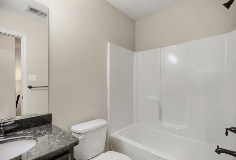 Bathroom featuring a white tub/shower combination, dark vanity with an integrated sink, and an undermount sink with a chrome faucet