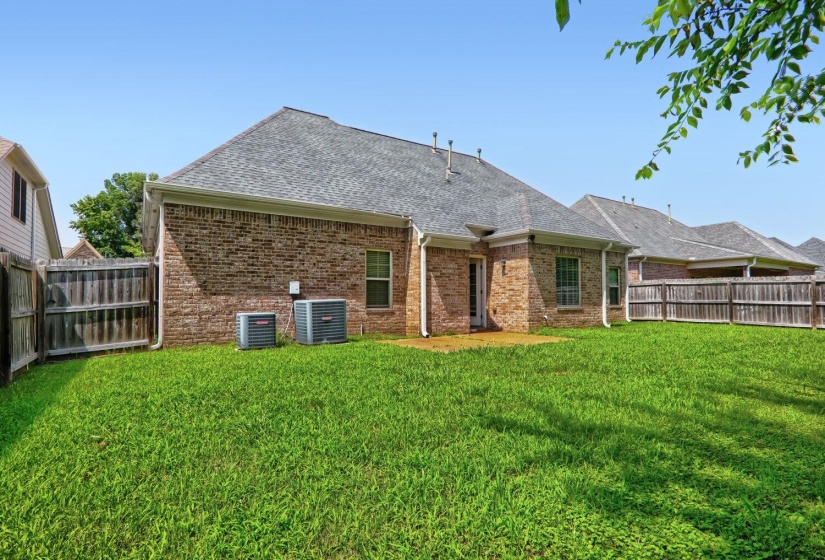 Expansive backyard featuring a manicured lawn, brick exterior, fenced perimeter, and a concrete patio