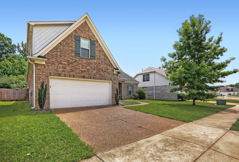 Brick facade home featuring a two-car garage, upper-level dormer window with shutters, and a gravel-finish driveway