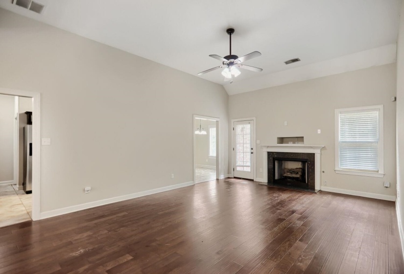 Vaulted ceiling living space featuring dark wood-finish flooring, a ceiling fan with integrated lighting, a fireplace with a dark stone surround and white mantel, and a glass-paned door