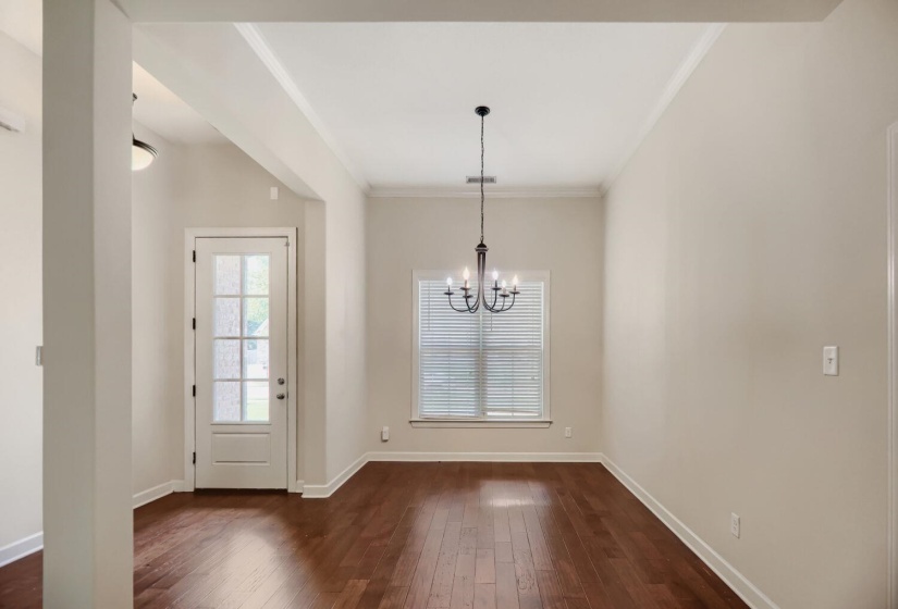Spacious room featuring wood-finish flooring, neutral wall tones, a transom window with blinds, and a classic chandelier