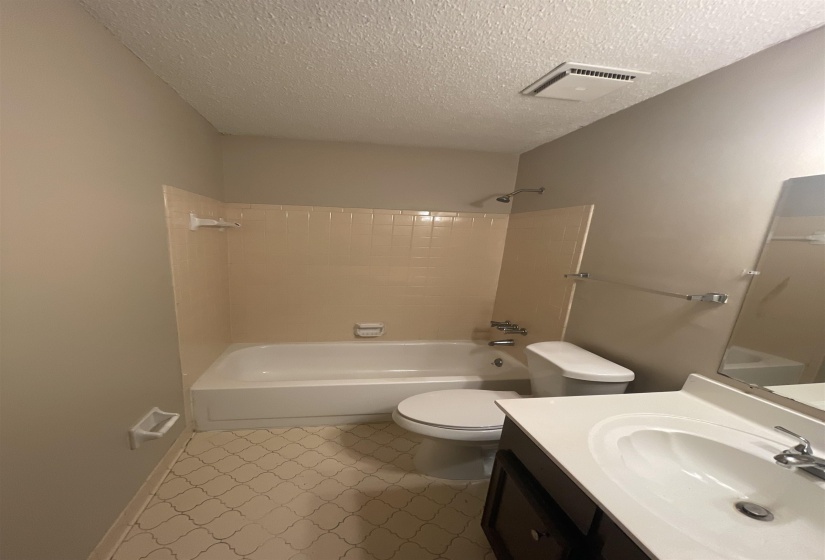 Bathroom featuring a white bathtub, beige wall tiling, patterned floor, and single vanity with a white countertop