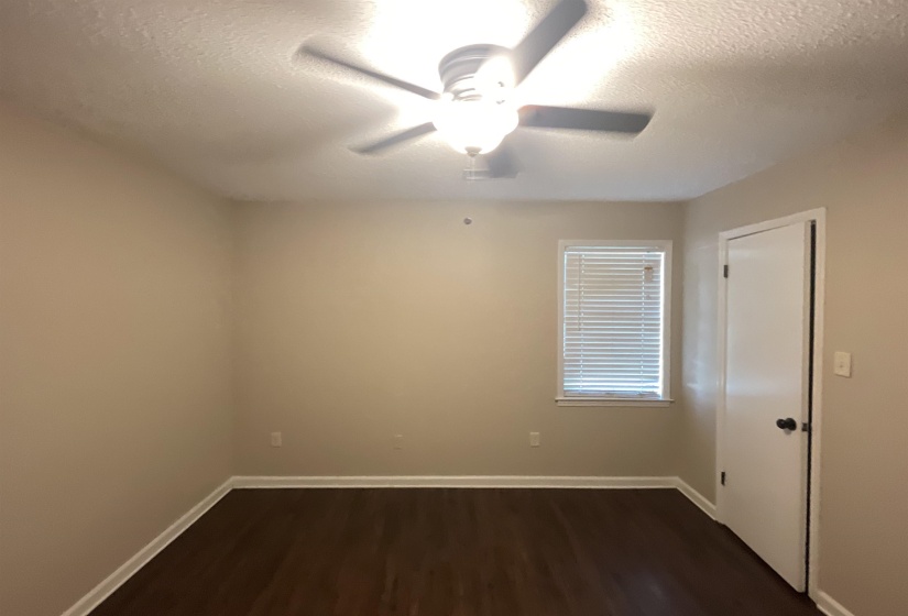 Spacious room featuring wood-finish flooring, light neutral wall tones, a ceiling fan with integrated lighting, and a window with blinds