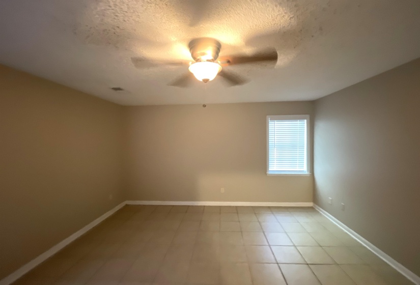 Spacious interior room featuring tile flooring, neutral wall paint, and a ceiling fan with integrated lighting