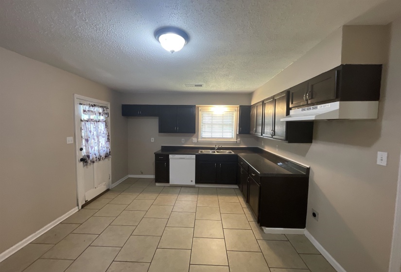Kitchen featuring dark wood cabinetry, a white dishwasher, stainless steel sink, and a white vent hood