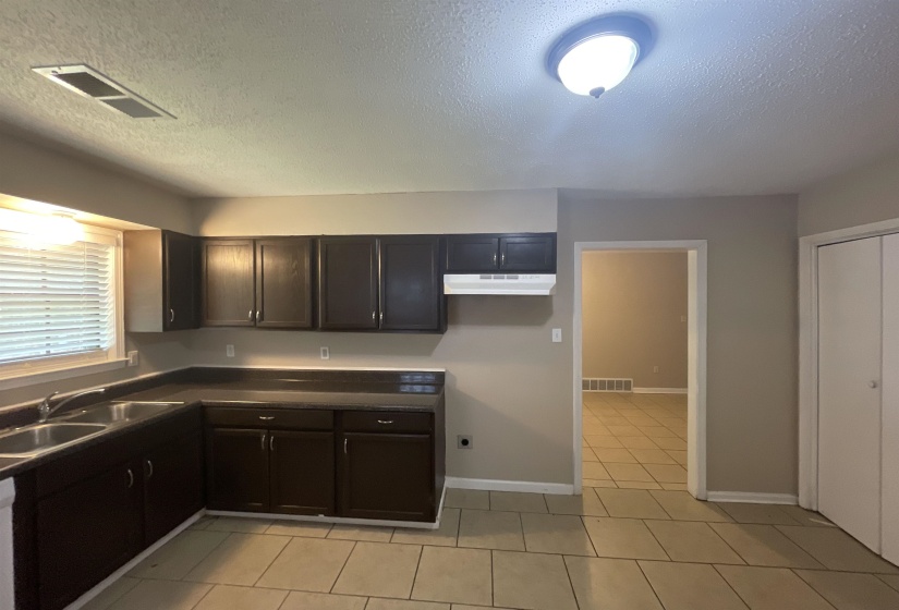 Spacious kitchen featuring dark wood cabinetry, a double basin stainless steel sink, ample countertop space, and neutral floor tiling