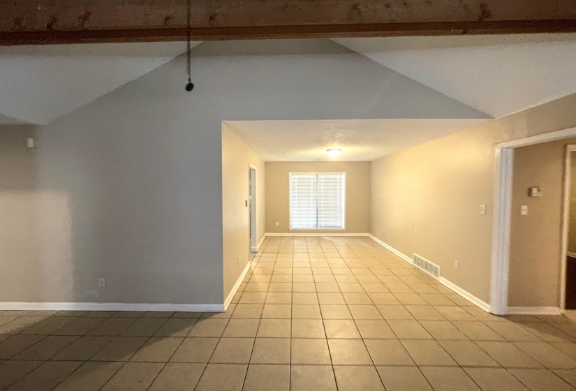 Spacious interior featuring a vaulted ceiling with exposed wood beam, tile flooring, and light neutral wall finishes