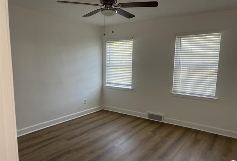 Room featuring wood-finish flooring, two windows with blinds, a ceiling fan with light fixture, and white baseboards