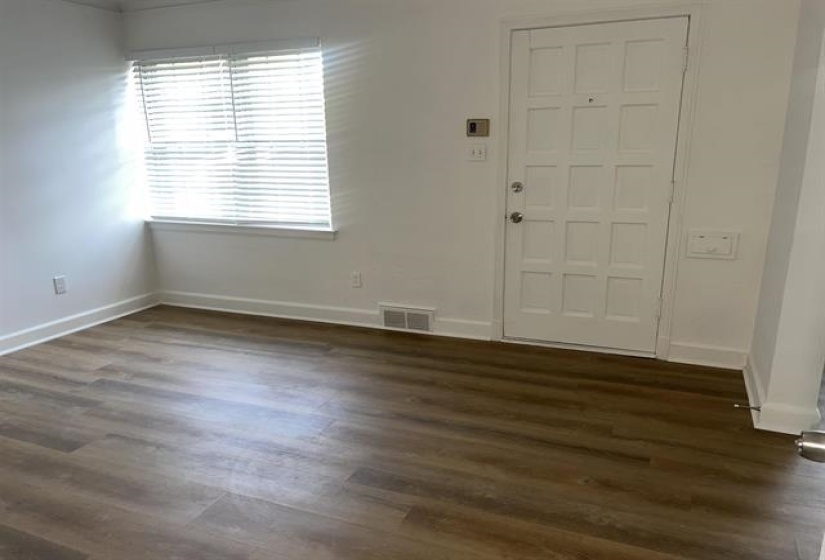 White paneled entry door with polished hardware, wood-finish flooring, white baseboards, and a window with blinds