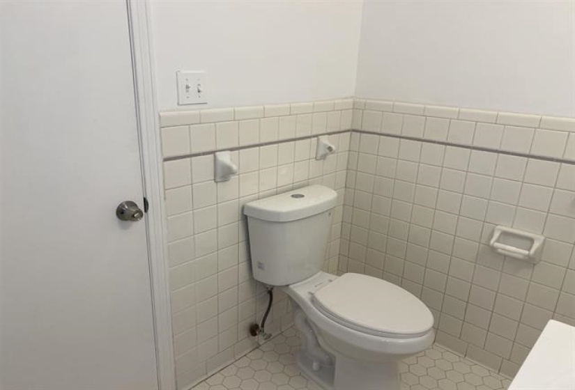 White toilet with a hexagon tiled floor and square wall tiles featuring a decorative accent line